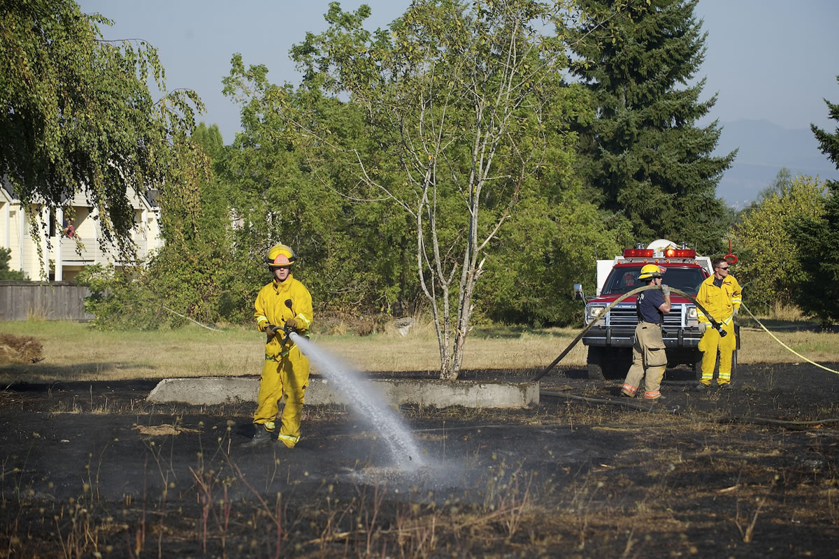 Firefighters water down the burned grass to prevent the fire from reigniting.