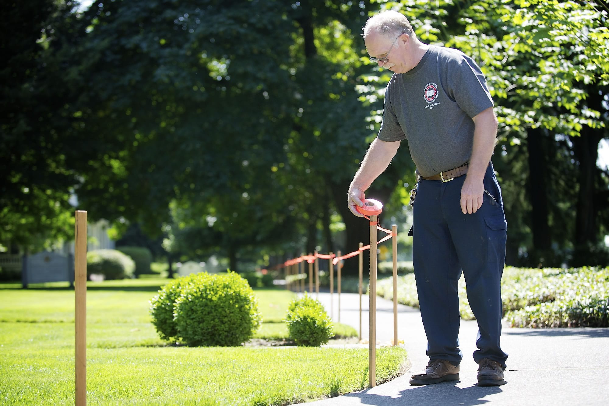 Fred Munhoven, a historical preservation specialist for the Fort Vancouver National Trust, sets up a tape barrier along Officers Row Tuesday as part of preparations for Independence Day at Fort Vancouver. Munhoven says he typically works 16 to 18 hours on the Fourth of July staring at 6 a.m.