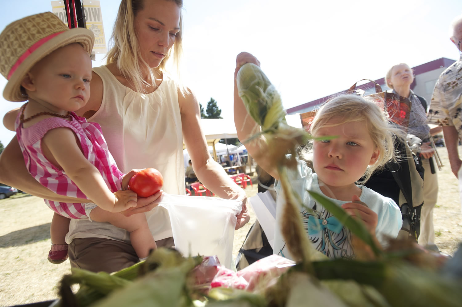 Four-year-old Ava Bond -- with her mom, Alexis, and 1-year-old sister, Sawyer -- picks out ears of corn at the Salmon Creek Farmers' Market on Thursday.