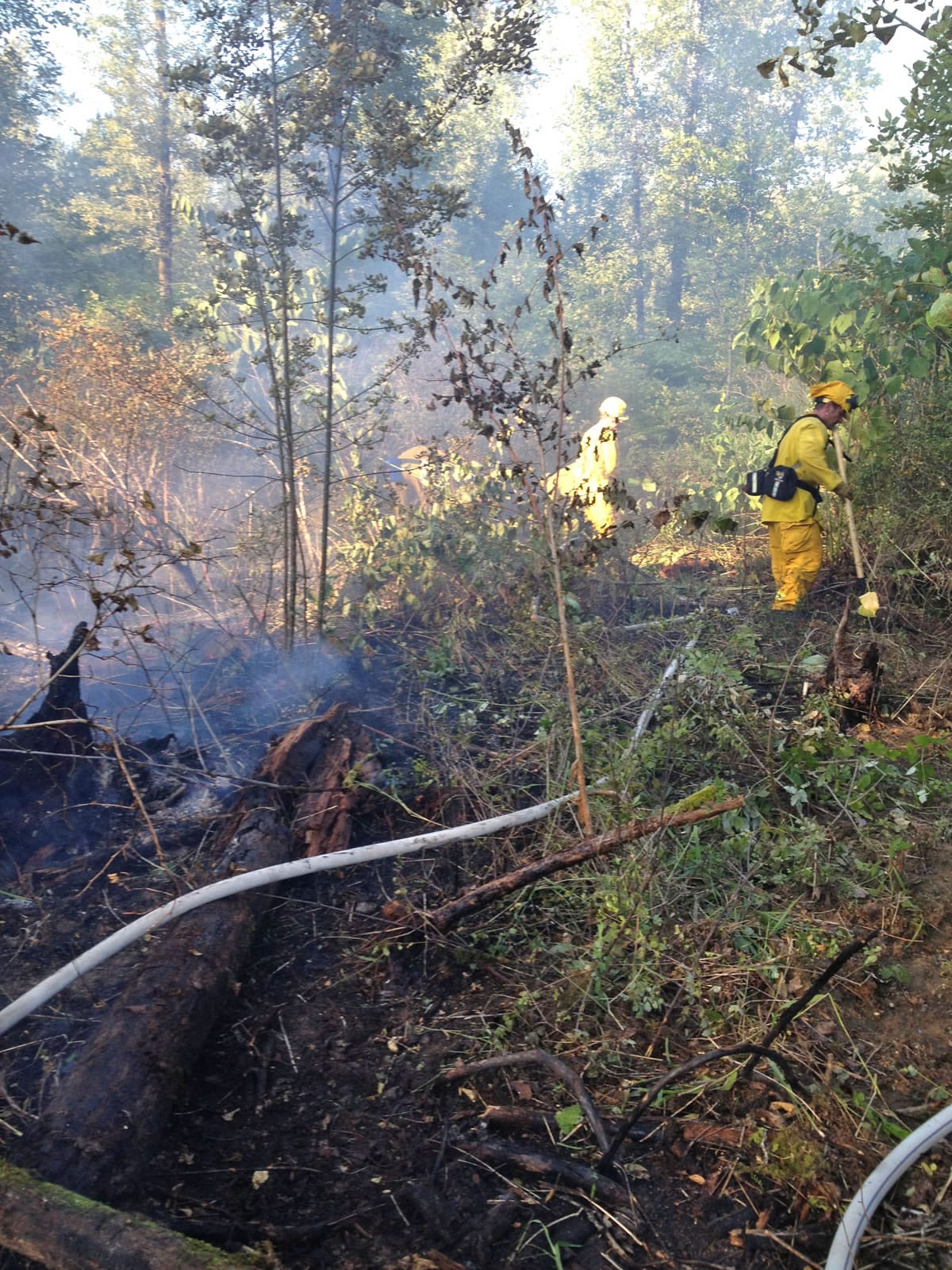 Firefighters hose down a forest fire that burned through nearly 2 acres Tuesday evening in north Clark County along the East Fork Lewis River.