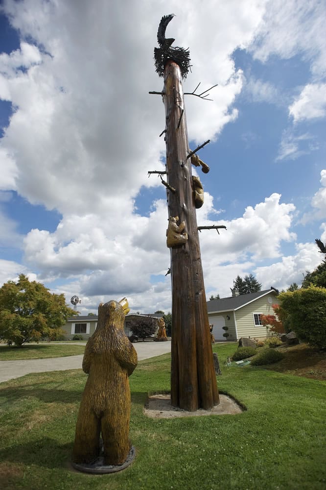 A carved momma bear looks up at a carved cub reaching for a honeycomb on an artist-made tree topped with a metal eagle sculpture made by a Boise, Idaho, artist.