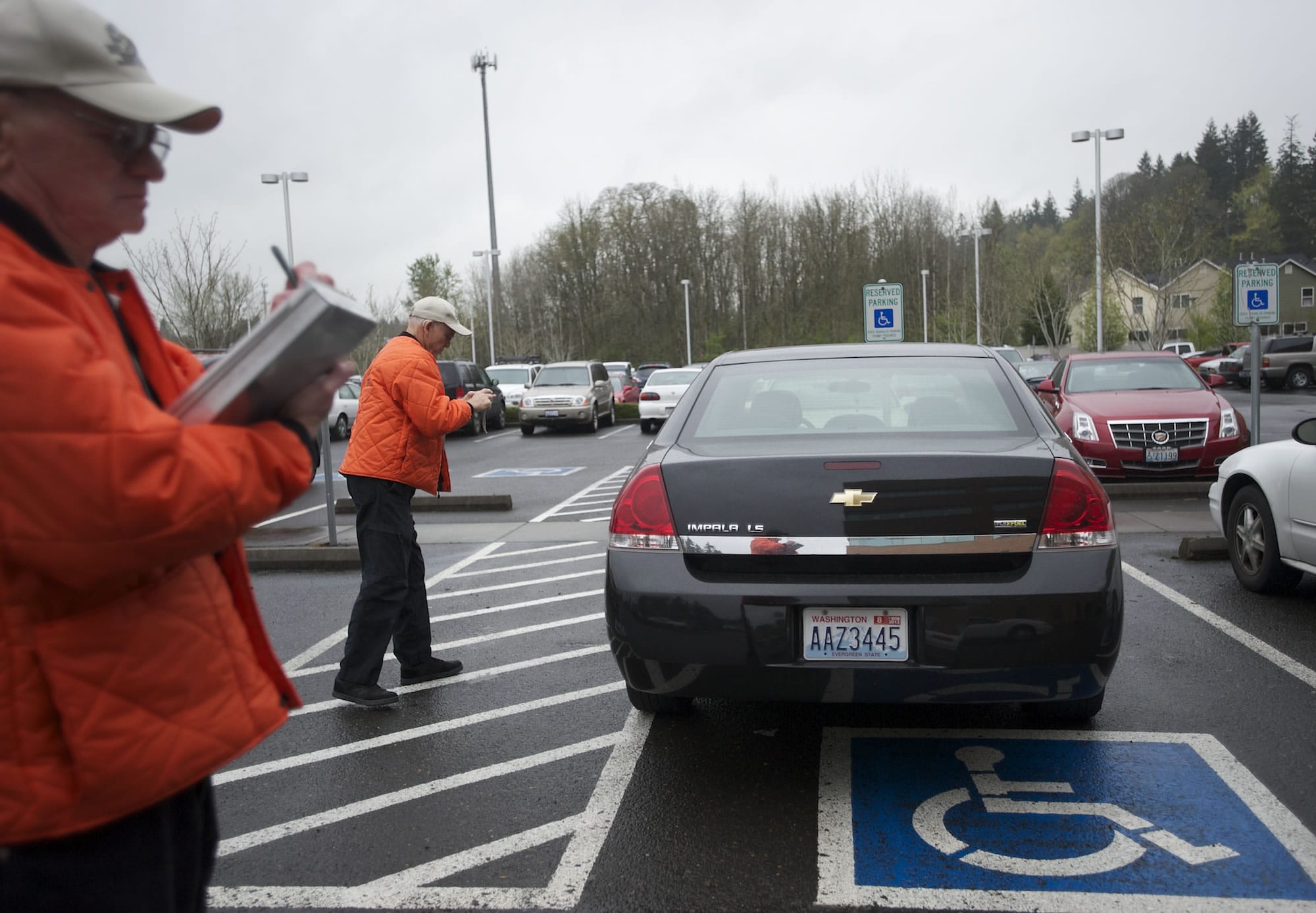 Parking enforcement volunteer Tom Croley, right, takes photos as his partner Gary Anderson writes out a ticket during a recent patrol in the Legacy Salmon Creek lot.