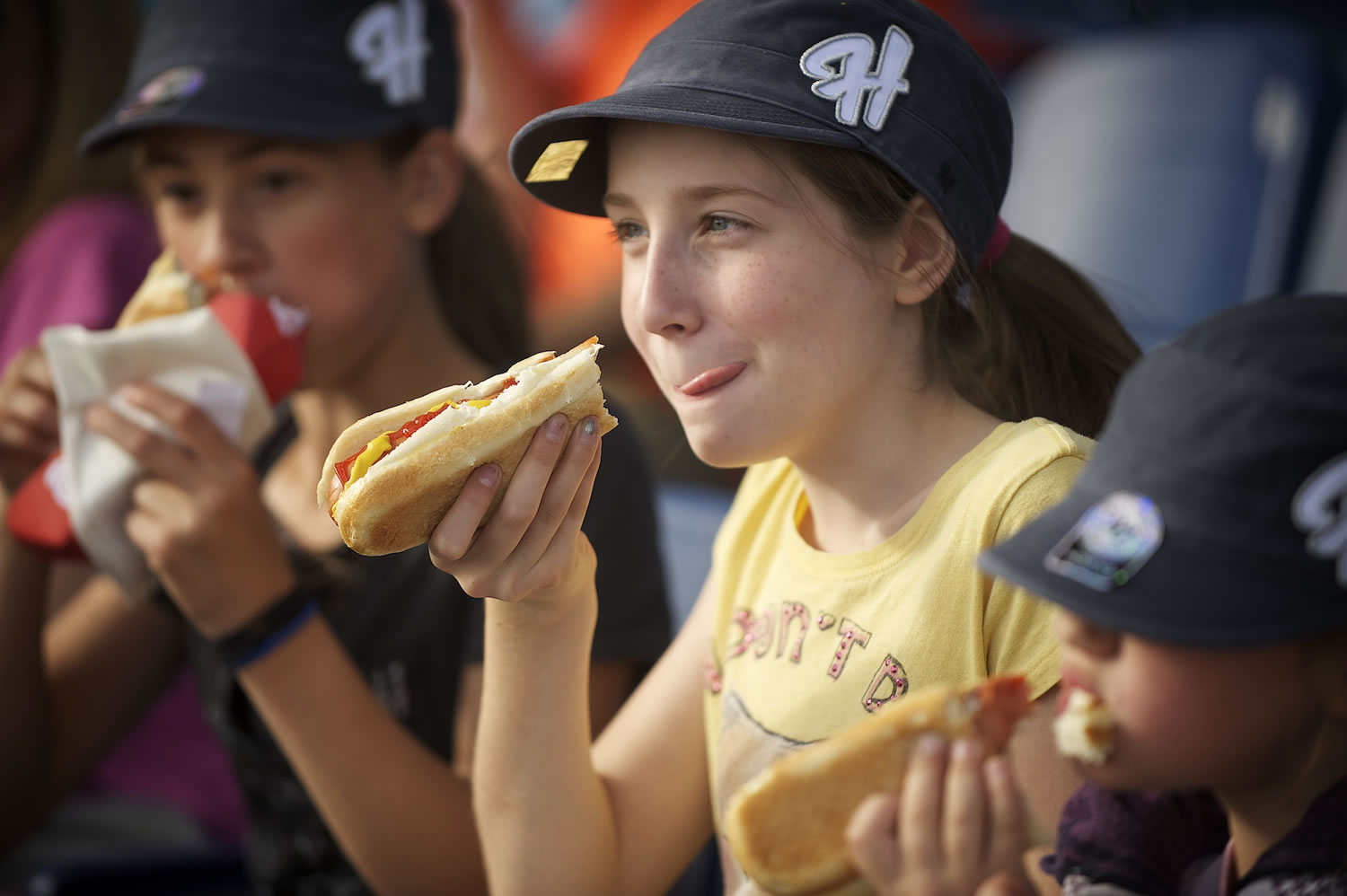 Sierra Carter, center, of Vancouver, enjoys a hot dog with her sisters during the home opener for the Hillsboro Hops against the Eugene Emeralds at Hillsboro Ballpark.