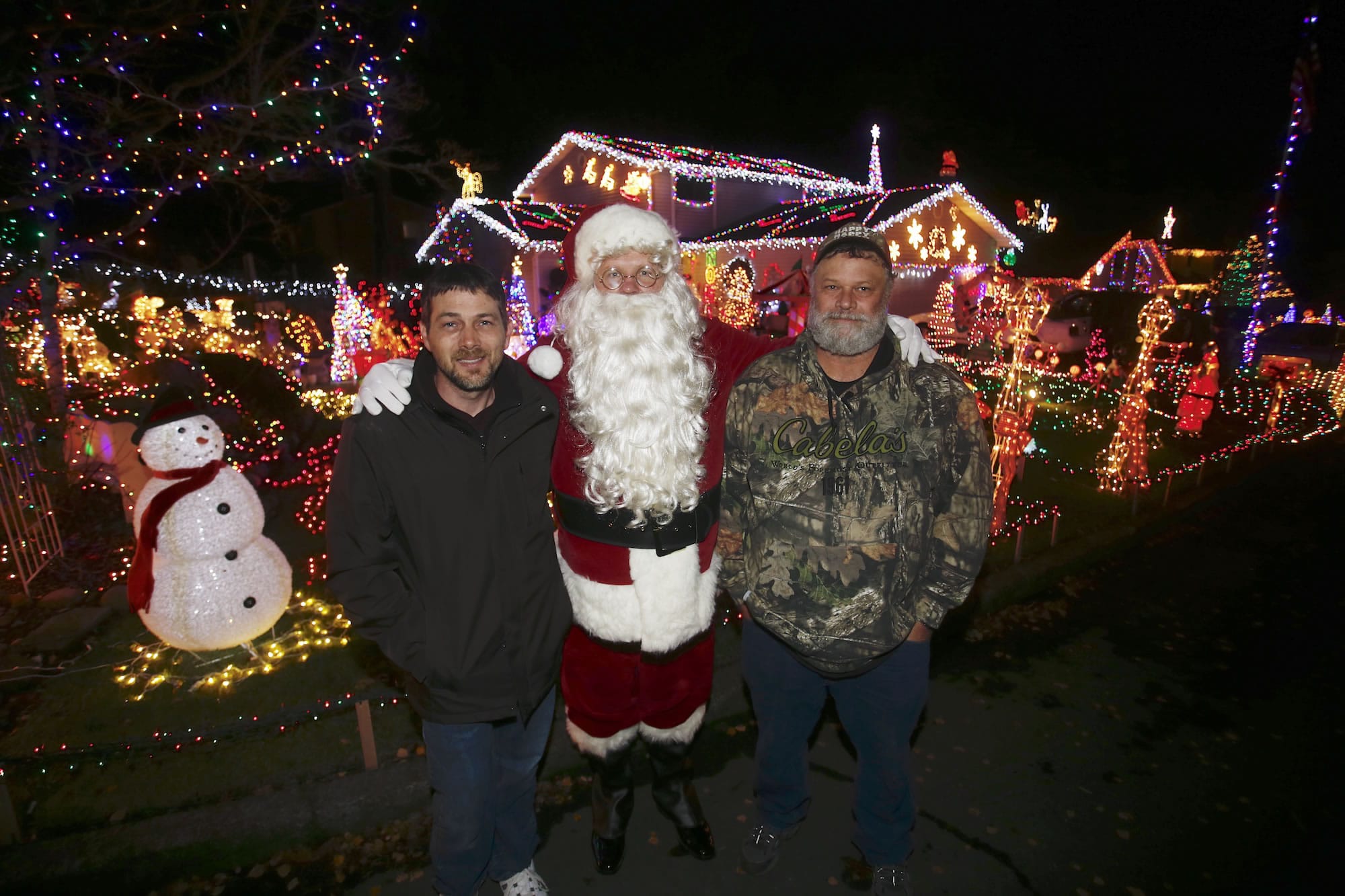 Randy Peppers, from left, David Buffum (dressed as Santa) and Paul Lamb have a friendly competition to show who can put up the most elaborate Christmas decorations at their homes on Southeast Riveridge Drive.