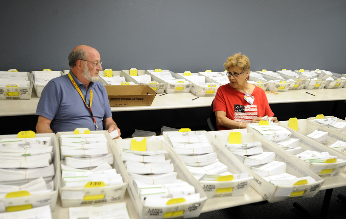 Election officers Josie Karling, right, and Gay Lincoln sit among ballots on Tuesday at the Clark County Elections Office in Vancouver. The vote-by-mail, top-two primary elections took place on Tuesday, and the general election is Nov.