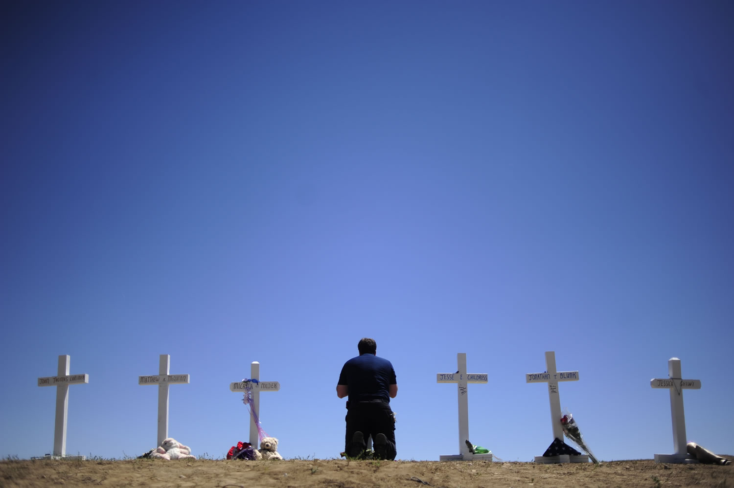 Travis Hirko kneels Sunday in front of the cross for Alex Sullivan at a memorial at in Aurora, Colo. Hirko went to high school with Sullivan, a victim of Friday's shooting rampage.