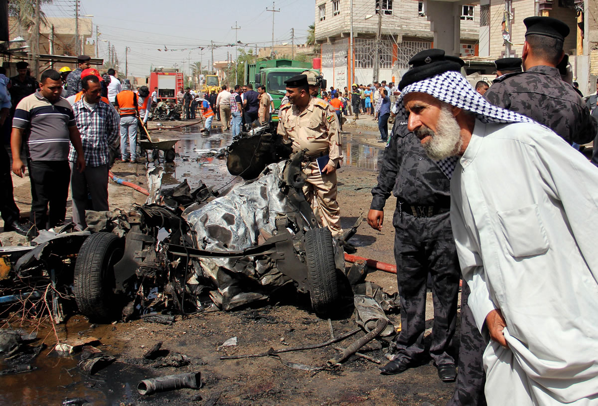 An Iraqi man and Iraqi security force members inspect the site of a car bomb attack Sunday in Basra, 340 miles southeast of Baghdad, Iraq.