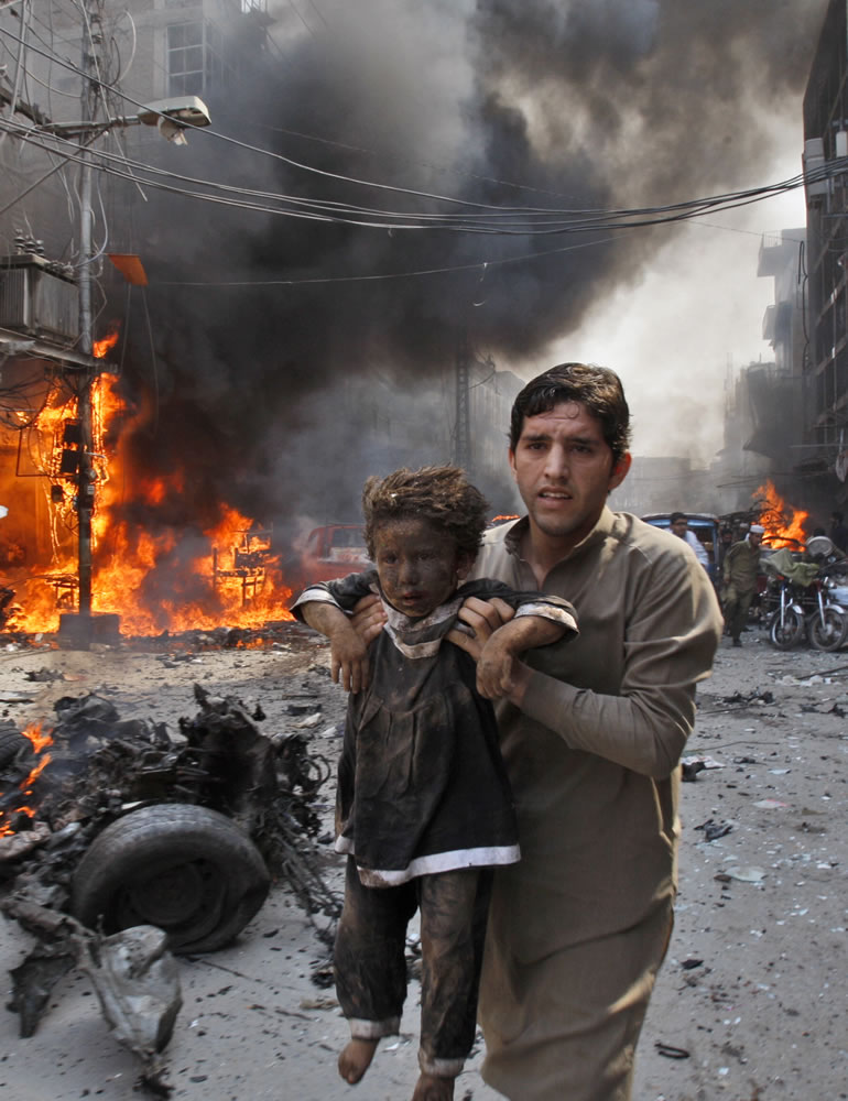 A man carrying a child Sunday rushes away from the site of a blast shortly after a car bomb exploded in Peshawar, Pakistan.