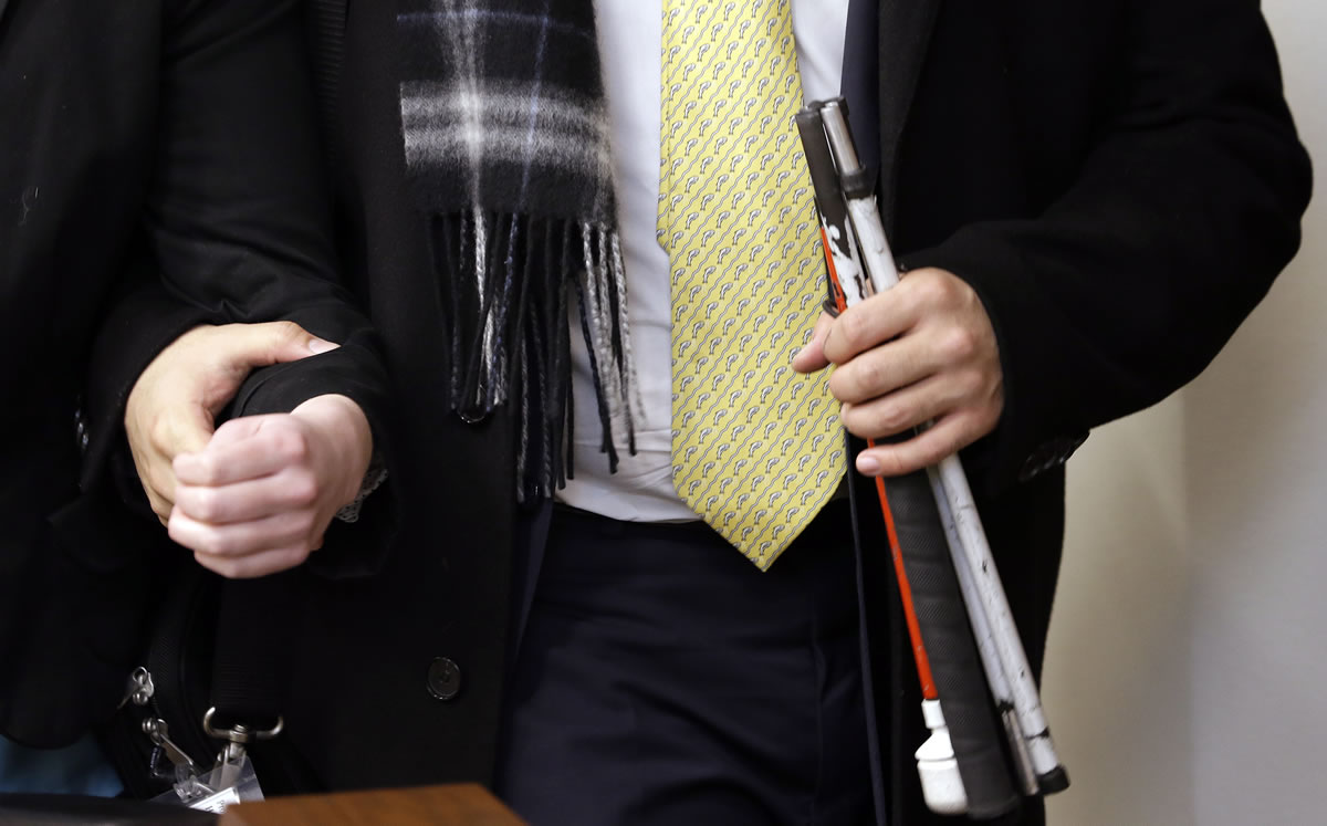 Rep. Cyrus Habib, D-Kirkland, holds his folded cane as he takes the arm of a legislative assistant as they leave a committee hearing in Olympia.