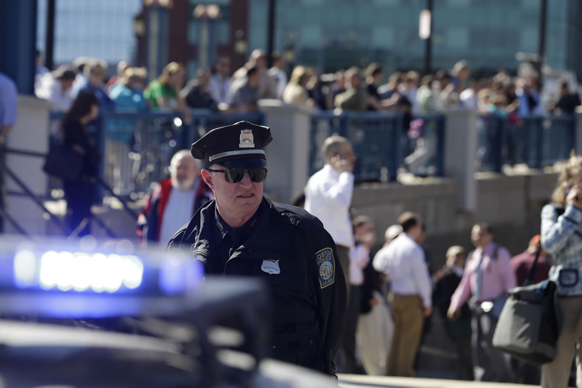 A Boston police officer stands guard as people stand on a bridge outside the John Joseph Moakley Federal Courthouse, which was evacuated amid conflicting reports that a suspect in the deadly Boston Marathon bombing is in custody Wednesday. The FBI and the U.S.
