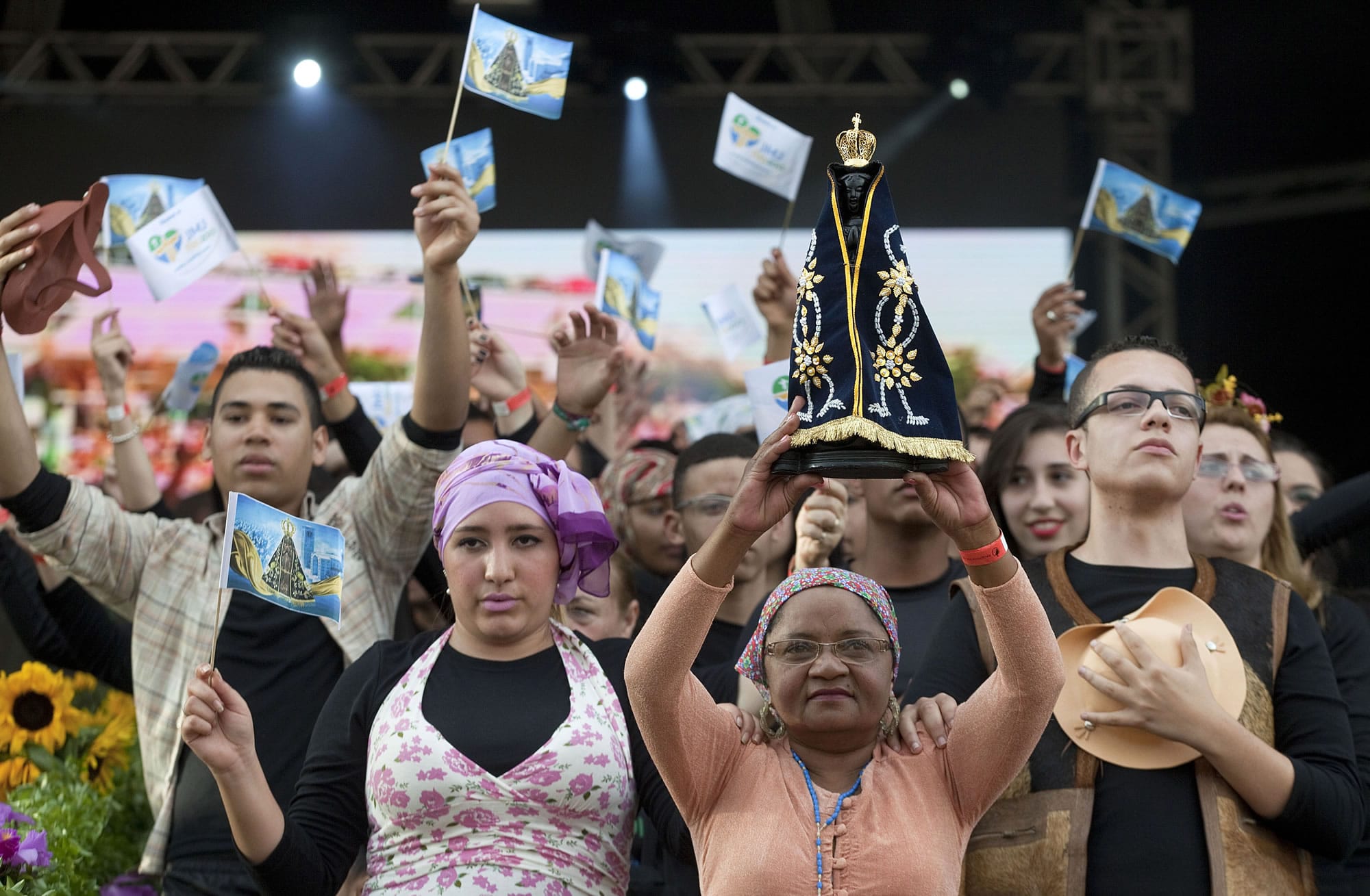 A woman holds up a replica of the statue of the Virgin of Aparecida as others wave flags with her image at a Mass ahead of World Youth Day in Sao Paulo, Brazil.