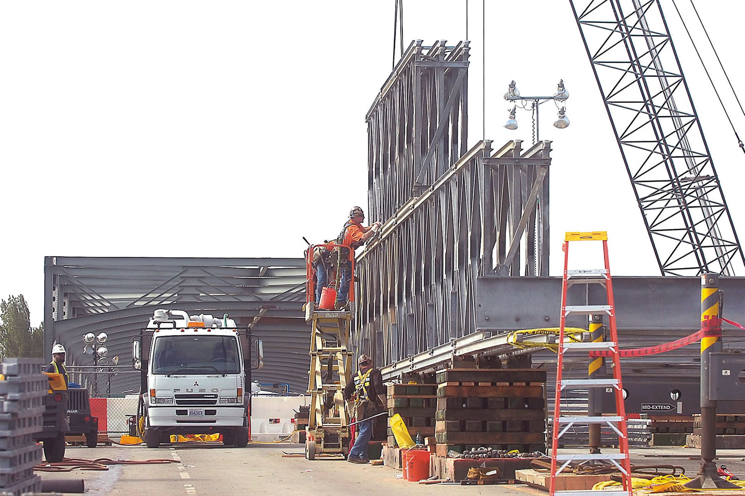 Construction crews on the north side of the fallen Skagit River Bridge work Monday to assemble girder sections for a temporary bridge span.