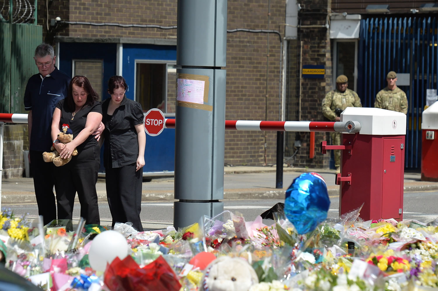 The mother of killed Drummer Lee Rigby, Lyn Rigby, center, holds a teddy bear as she joins his stepfather, Ian, and other family members look at floral tributes outside Woolwich Barracks as they visit the scene of Lee Rigby's murder in Woolwich, south-east London, on Sunday.