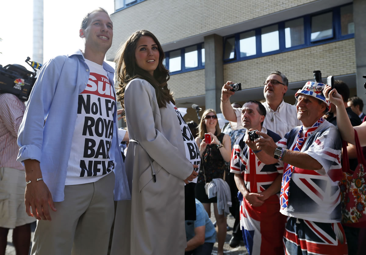 Royal supporters, right, look on as a couple impersonate  Britain's Prince William and Kate, the Duchess of Cambridge as they pose for photographers, during a publicity stunt for a daily newspaper, outside St.