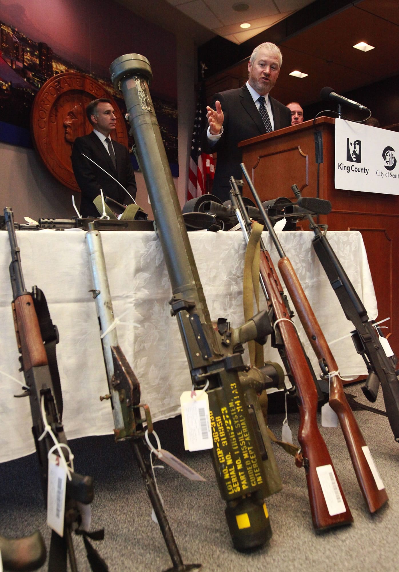 Seattle Mayor Mike McGinn, right, addresses a news conference Monday in Seattle. A missile launcher, front center, was found during a weapons buyback event Saturday.