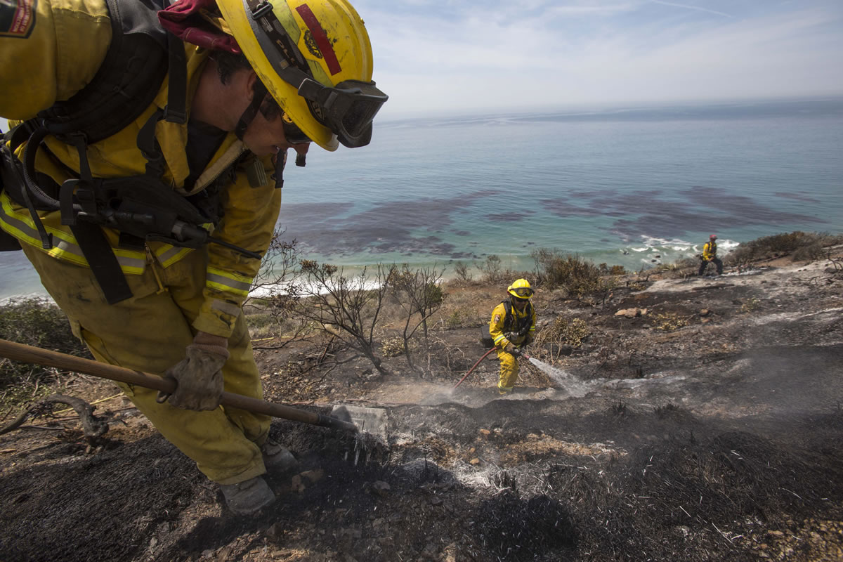 Firefighters work on the burned area Friday along the Pacific Coast Highway, in Point Mugu, Calif. A huge wildfire carved a path to the sea and burned on the beach Friday, but firefighters got a break as gusty winds turned into breezes.