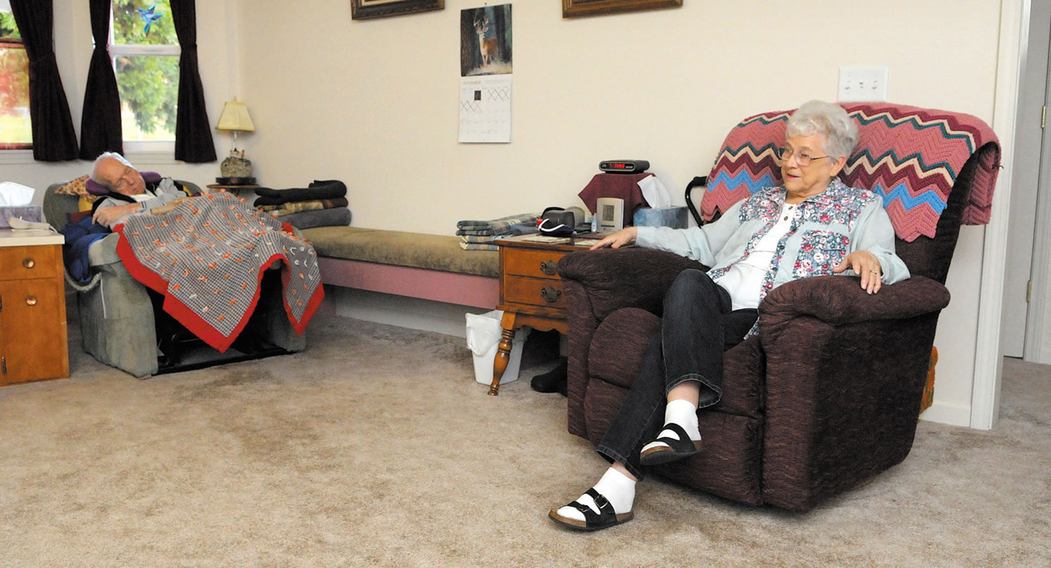 LouVee Walker, 75, talks to a visitor in her Sweet Home, Ore., home as her husband, Jim, dozes nearby. LouVee is the caregiver for her husband, who has Lewy body dimentia. The condition has left him immobile and needing constant care.