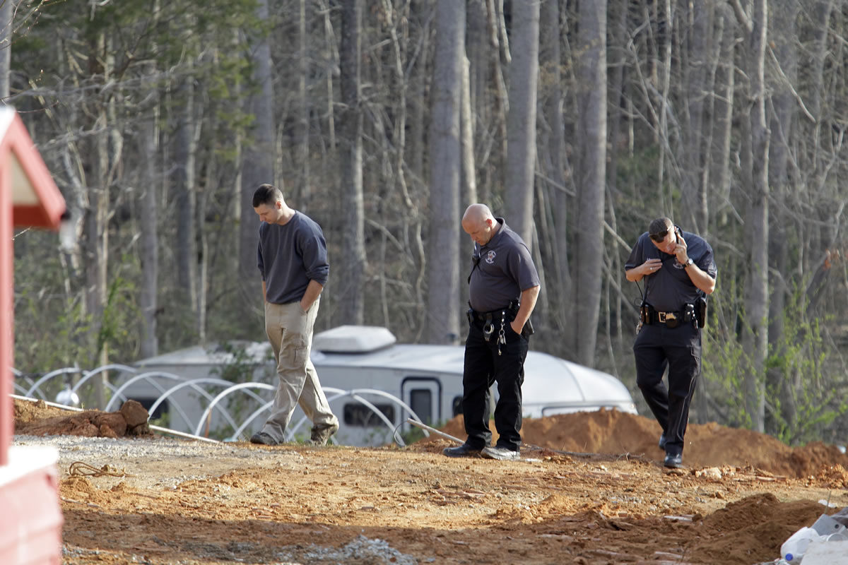 A man, left, walks with investigators Monday around the scene of a collapsed construction site where two children died when the dirt walls collapsed Sunday on Cedarbrook Court in Stanley, N.C.