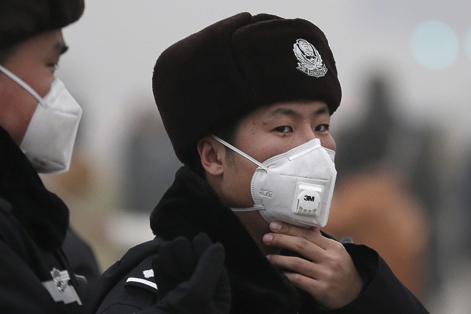 A policeman adjusts his mask Tuesday as he and his colleagues patrol near Tiananmen Gate in Beijing. Schools in the Chinese capital kept students indoors and parents brought their kids to hospitals with breathing ailments Tuesday as Beijing grappled with severe air pollution.