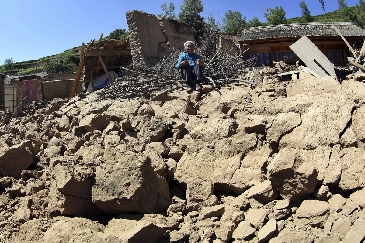 A woman sits on the remnants of a quake destroyed house in Lalu village of Hetuo township in Minxian in northwest China's Gansu province Monday July 22, 2013.  A strong earthquake that shook an arid, hilly farming area in northwest China sparked landslides and destroyed or damaged thousands of brick-and-mud homes Monday, killing at least 75 people and injuring more than 400, the government said.