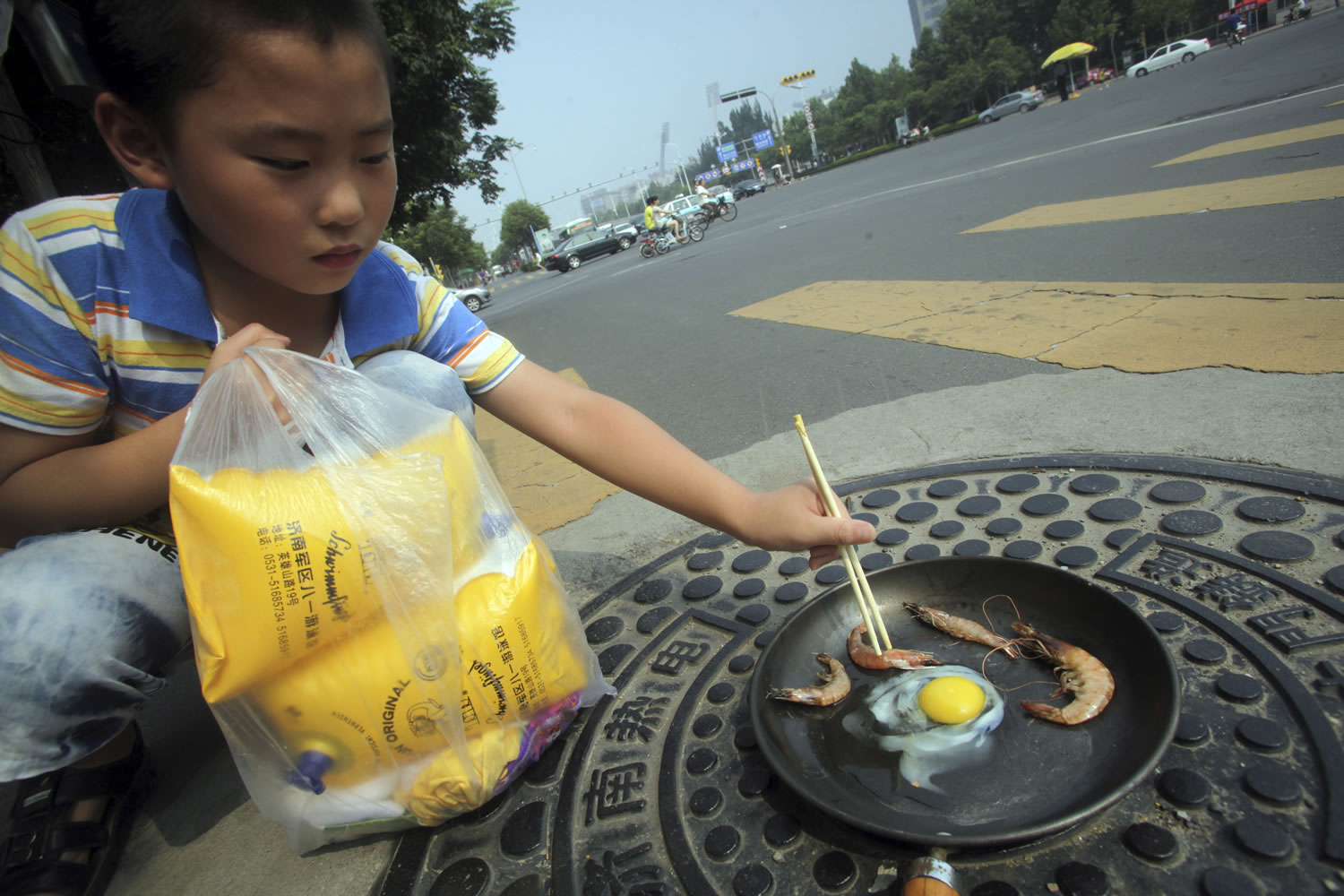 A child tries frying raw shrimp and an egg in a pan on a manhole cover Wednesday in Jinan, China.