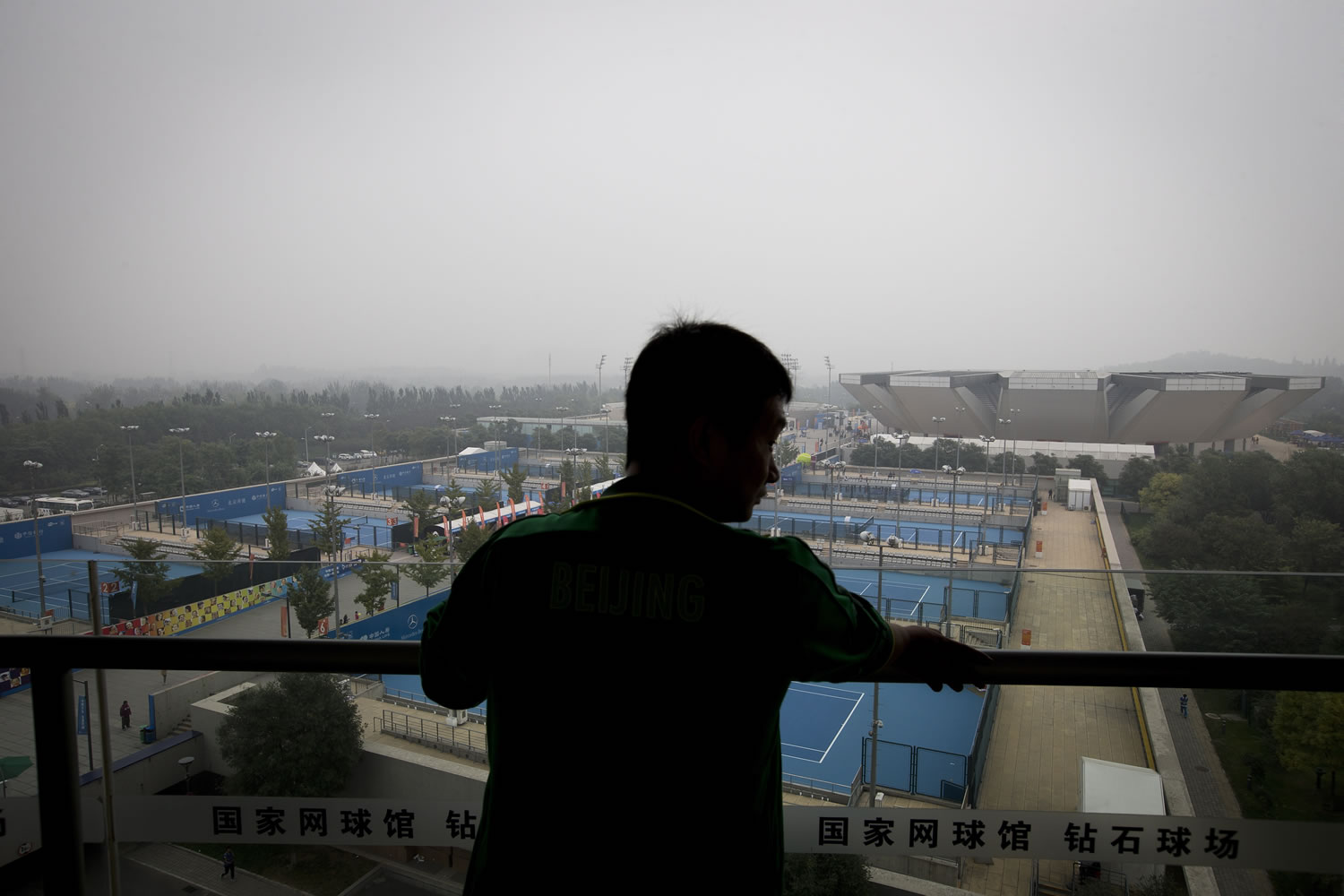 A man stands on the balcony of National Tennis Stadium looks at the tennis courts shrouded by haze in Beijing.