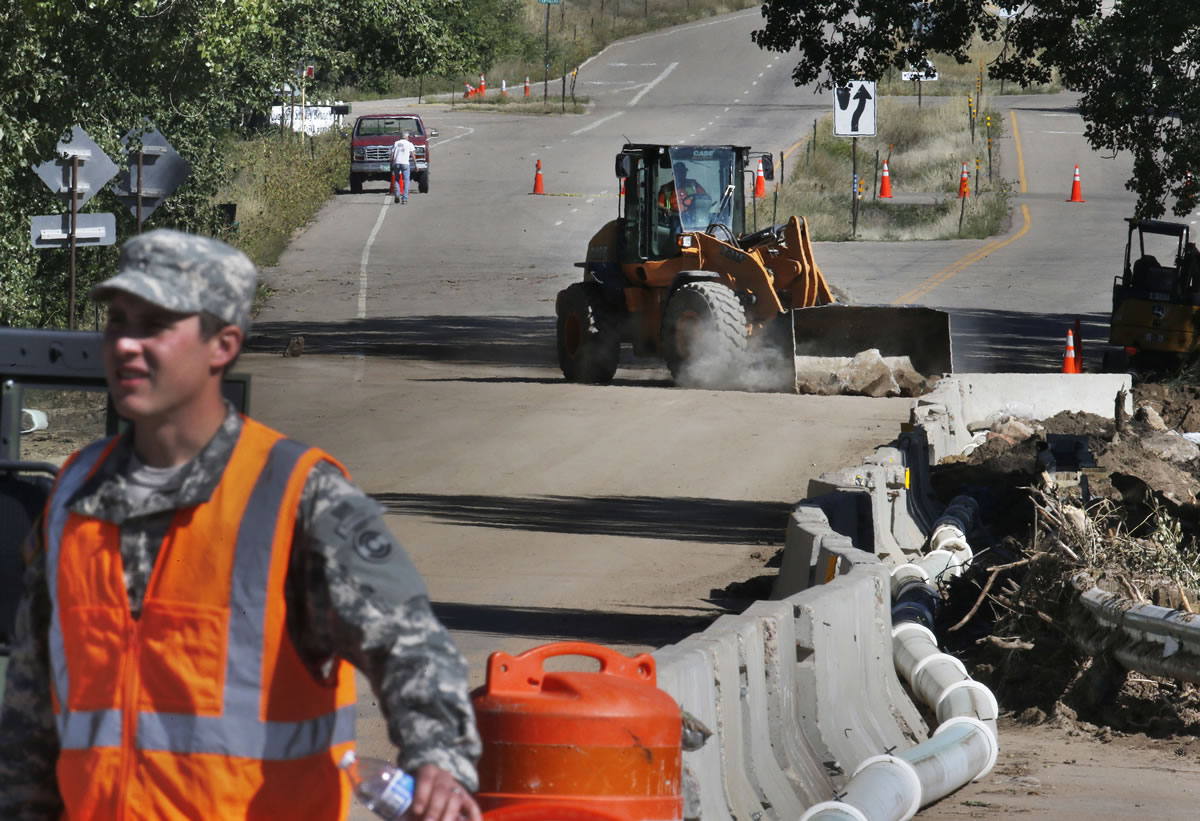 A National Guard soldier mans a roadblock Friday as a bulldozer clears concrete flood debris from a damaged road being repaired after last week's flood, west of Longmont, Colo. With snow already dusting Coloradois highest peaks, the state is scrambling to replace key mountain highways washed away by flooding.