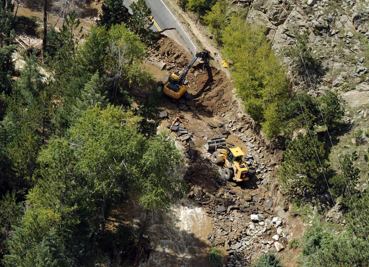 Heavy equipment works on a road damaged by flooding during a helicopter search of the area around Boulder, Colo.