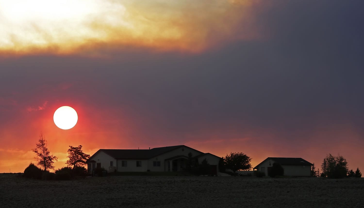 The sun sets through wildfire smoke Sunday near Monte Vista, Colo.