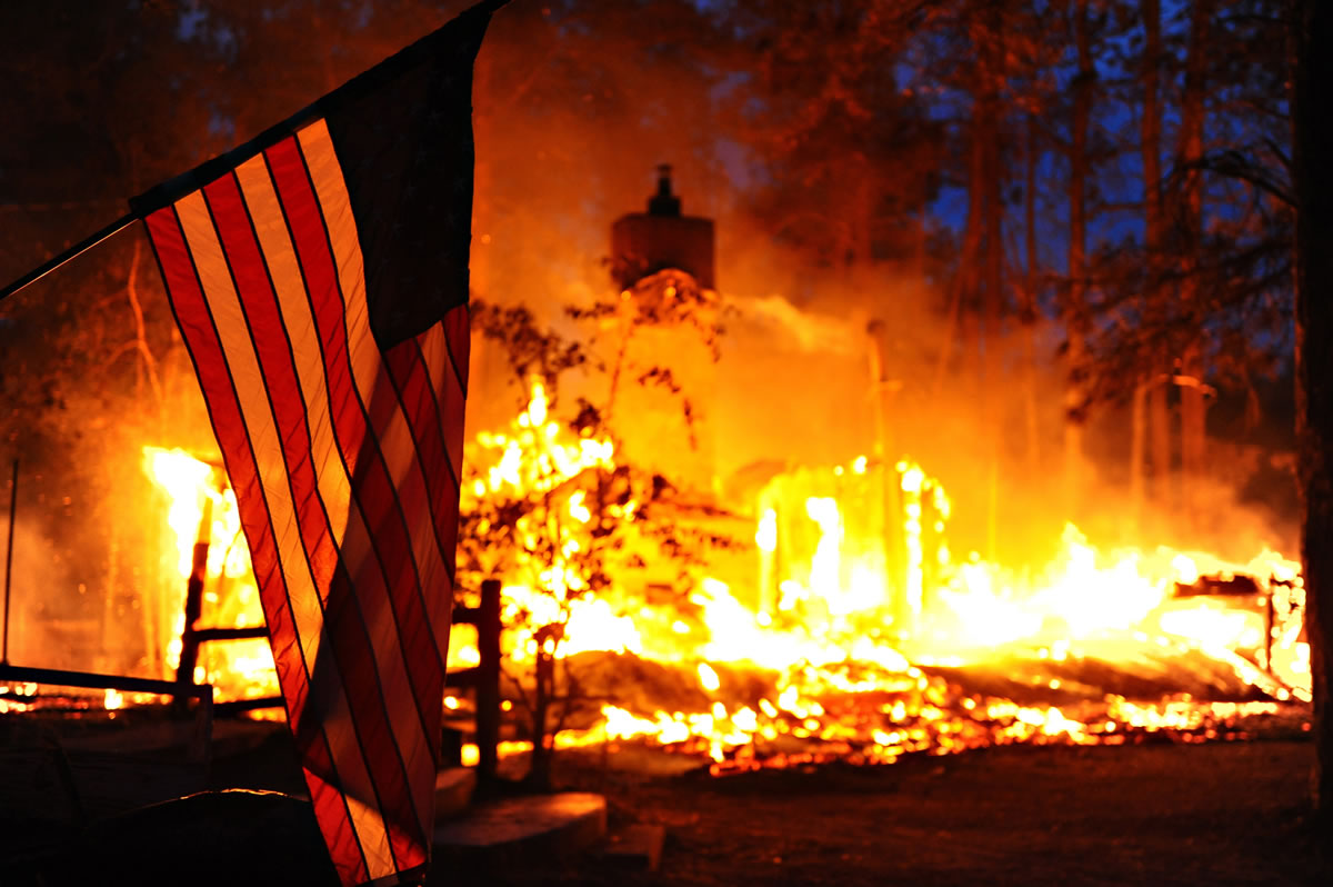 In this Tuesday photo, released Saturday, by the U.S. Air Force, an American flag hangs in front of a burning structure in the Black Forest, a thickly wooded rural region north of Colorado Springs, Colo. Authorities reported early Saturday that 473 houses had been incinerated.