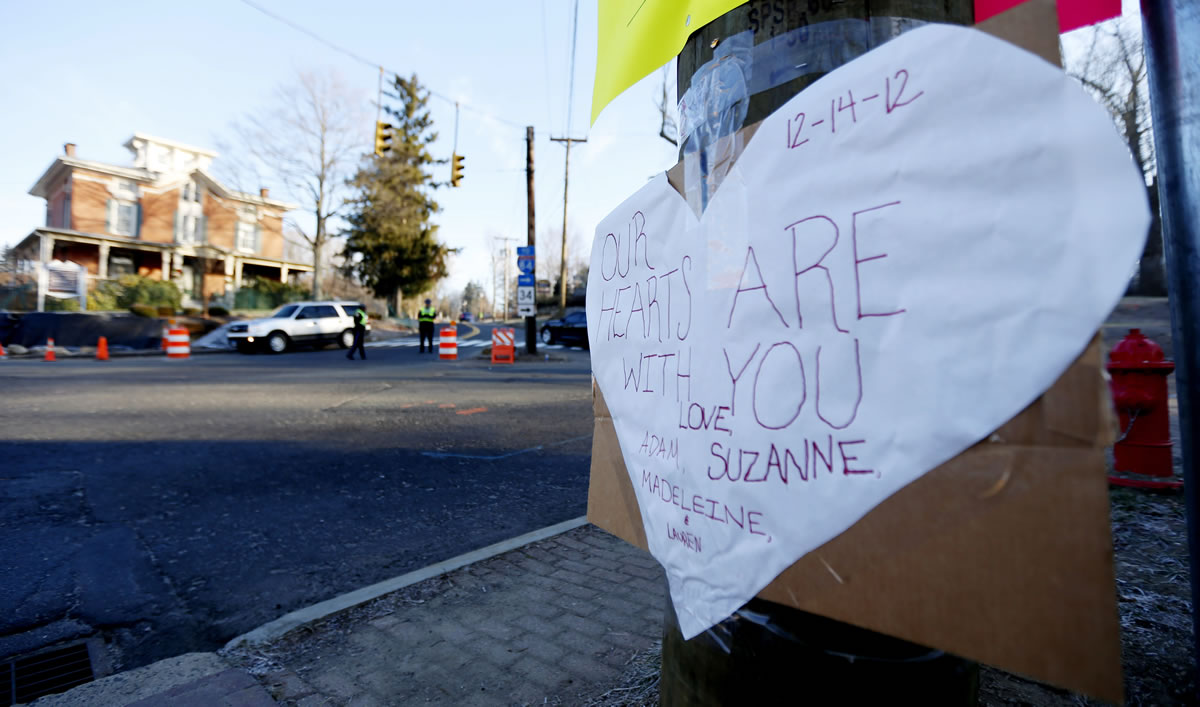 A sign on a post shows support for the victims of a gunman who opened fire inside Sandy Hook Elementary School a day earlier as police officers stand at a road block, Saturday, Dec. 15, 2012, in Sandy Hook village of Newtown, Conn.