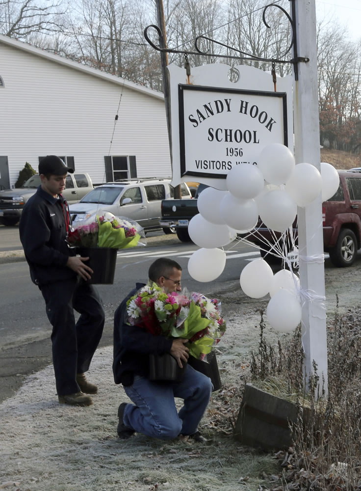 Volunteer firefighters place flowers at a makeshift memorial at a sign for the Sandy Hook Elementary school Saturday, Dec. 15, 2012 in the Sandy Hook village of Newtown, Conn. The massacre of 26 children and adults at Sandy Hook Elementary school elicited horror and soul-searching around the world even as it raised more basic questions about why the gunman, 20-year-old Adam Lanza, would have been driven to such a crime and how he chose his victims.