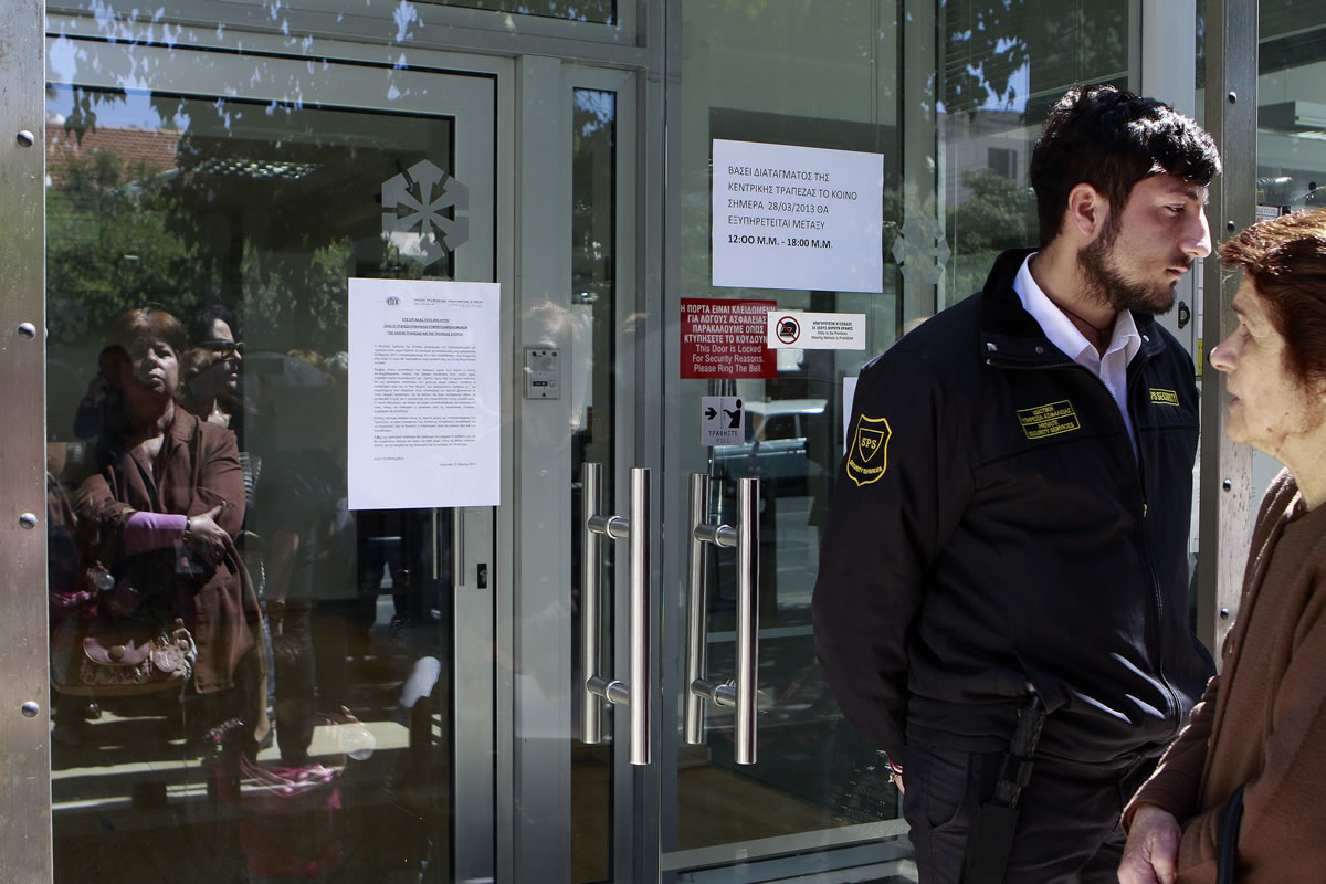 A private security services guard, right, stands in front of the bank's main door as people wait outside a branch of Laiki Bank in Nicosia on March 28.