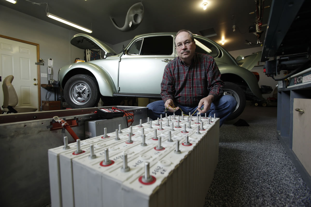Dean West poses with batteries for the 1974 Volkswagen Super Beetle he has converted to run on all-electrical power in the garage of his home in Milton.