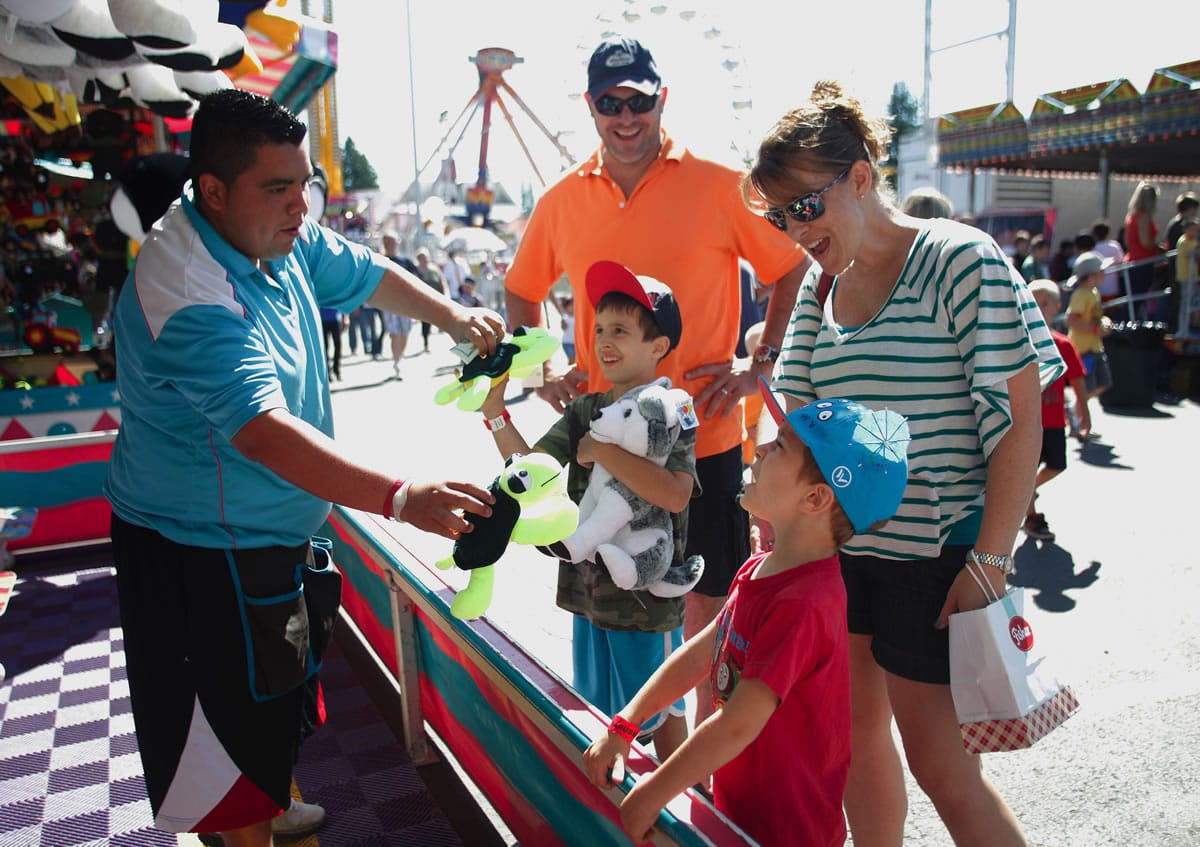Fredy Martinez hands prizes to Jake Krisvoshein, 7, who played the bucket toss game last month with parents, Todd and Dee, and brother Tyson, 5, right, at the Evergreen State Fair in Monroe.