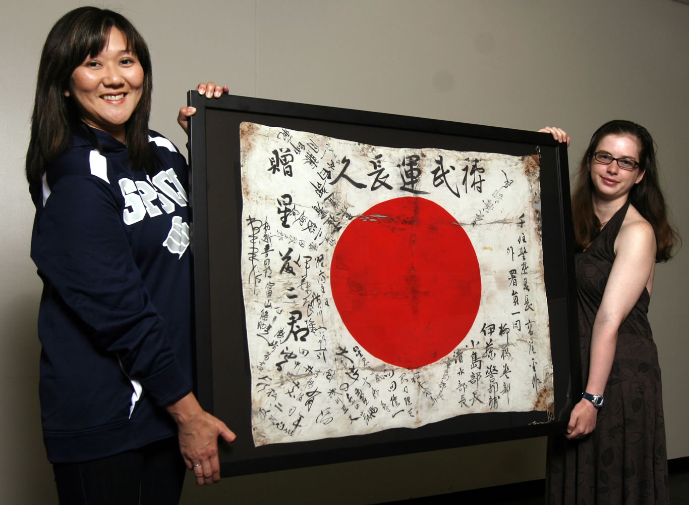 South Puget Sound Community College instructor Aki Suzuki, left, and Jennifer McDougall hold a Japanese flag McDougall's grandfather brought home from World War II.
