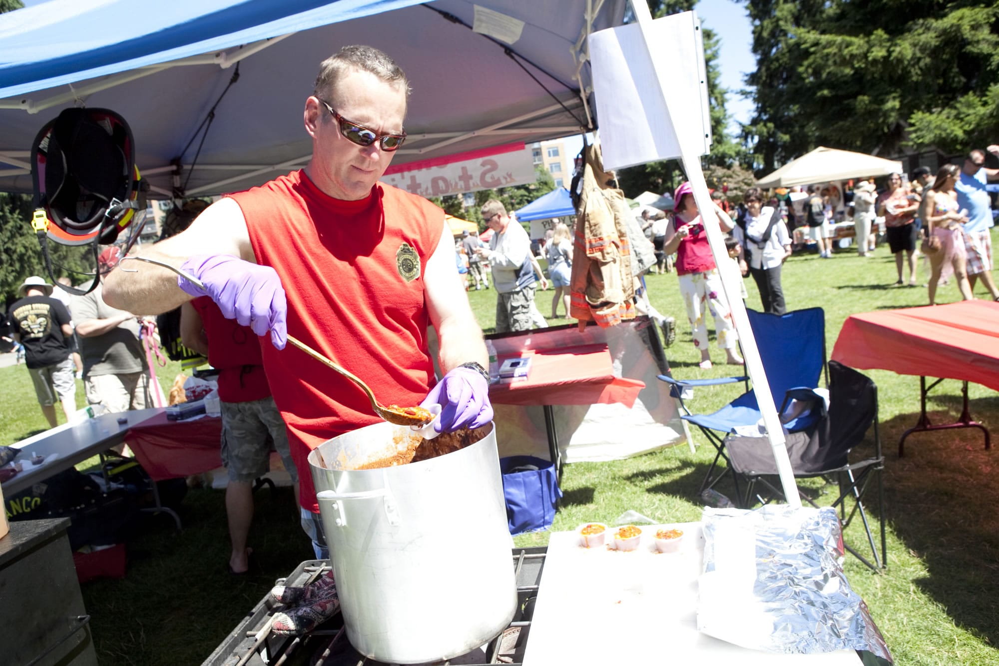 Drew Tracy of Station 8 pours samples of their Smoked Chicken Chipoltle Chili during The Fire Fighter's Chili Cookoff which brought large crowds of people to Esther Short Park Saturday afternoon to raise money for the homeless.