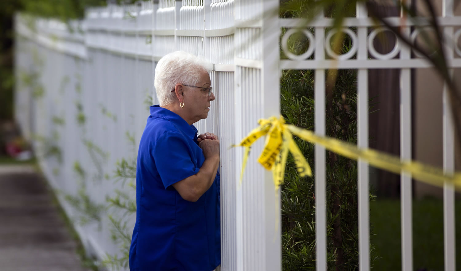An unidentified woman looks through a fence near a murder scene Thursday in Miami.