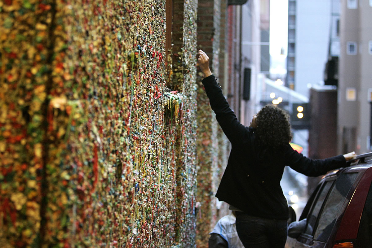 John Lok /The Seattle Times
Lorena Diaz contributes to the gum wall below Pike Place Market in Seattle. Located on Post Alley between Pike and Union streets, the wall is a well-known tourist attraction at the Market. Geotouring is a high-tech scavenger hunt that usually shows off a city's interesting and sometimes odd features.