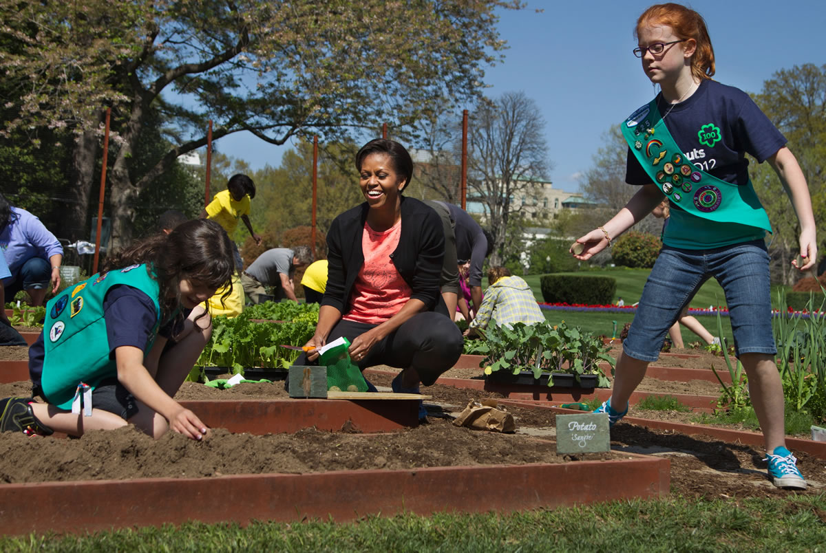 First lady Michelle Obama, center, laughs as she and Girl Scouts Gia Muto, left, and Emily Burnham, from Fairport, N.Y., plant potatoes during a spring planting of the White House kitchen garden at the White House in Washington in March 2012.