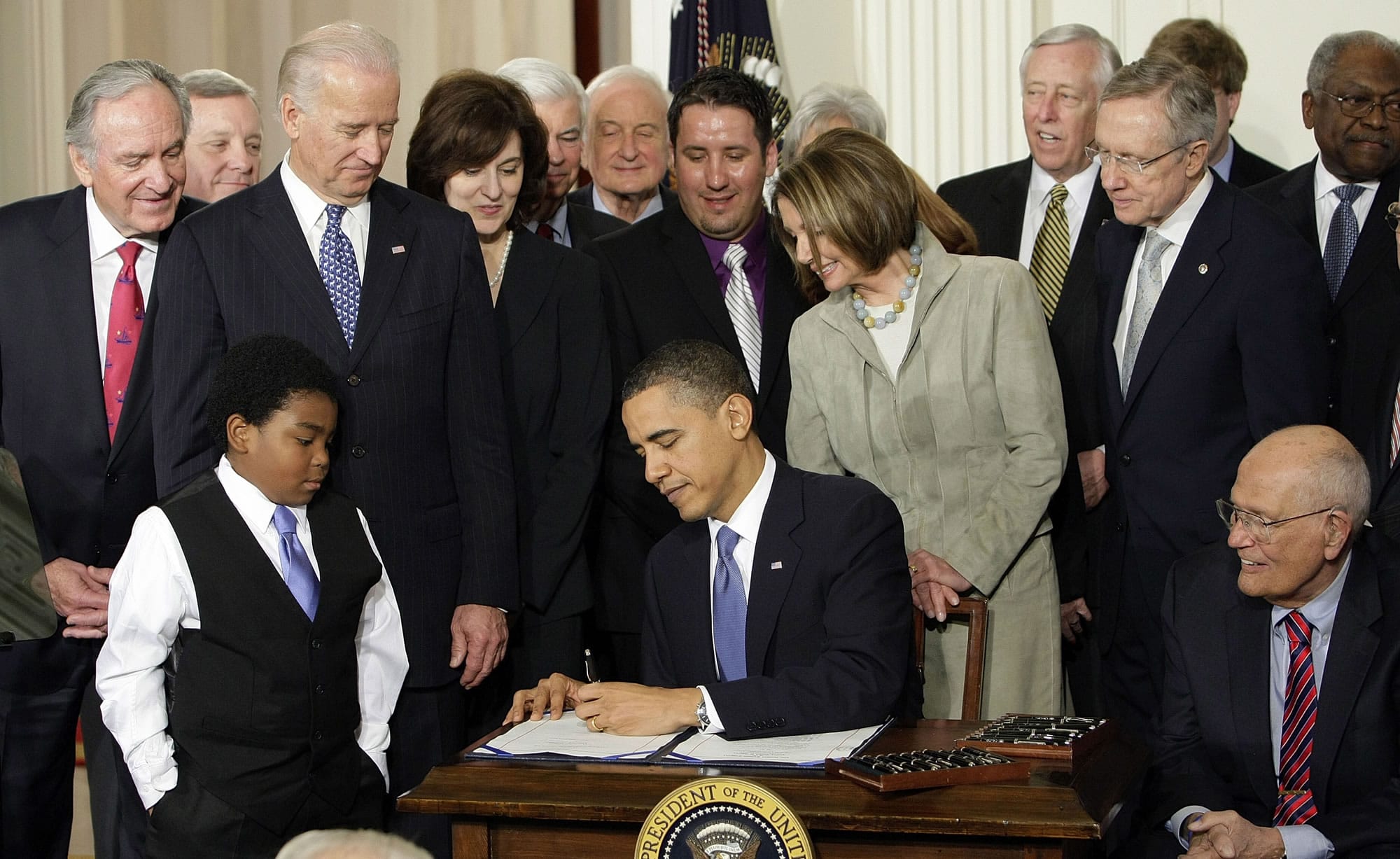 Officials and others look on as President Barack Obama signs the health care bill in the East Room of the White House in Washington on March 23, 2010. The first yearly sign-up period for the Patient Protection and Affordable Care Act closes Monday, with early returns suggesting the administration may near a projection of 7 million enrollees made before the U.S.