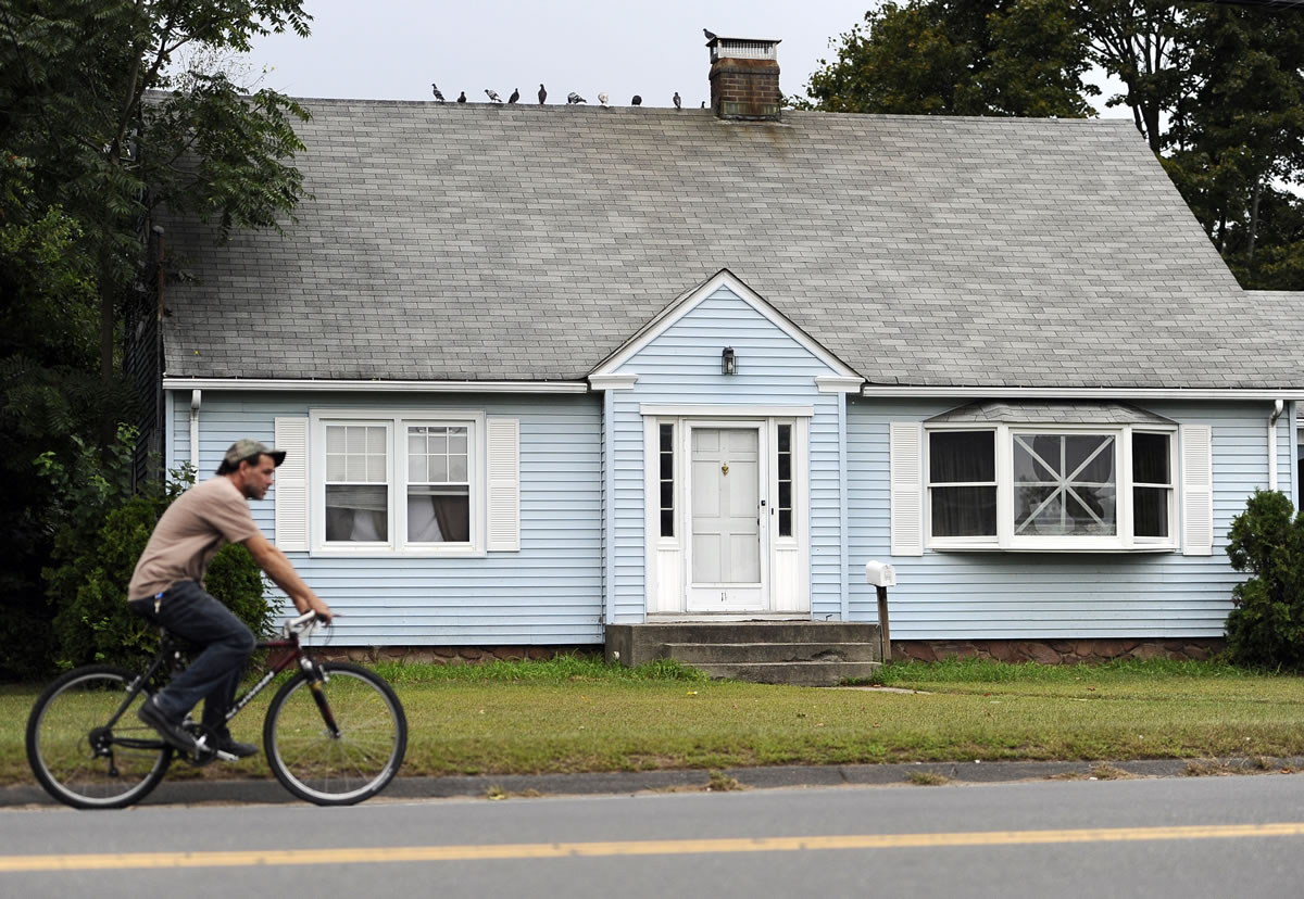 A man rides a bicycle past a house owned by the uncle of former New England Patriot's Aaron Hernandez on Thursday in Bristol, Conn.