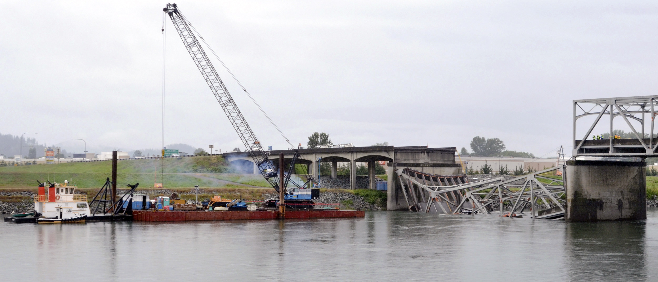 A view from the Mount Vernon side of the Skagit River shows a crane on a barge Sunday at the scene of the Interstate 5 bridge collapse in Washington.