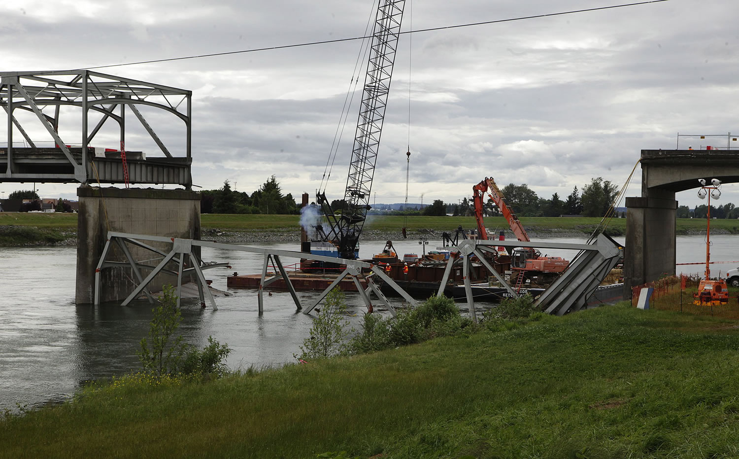 Construction workers wait as divers check out the deck of the bridge down below the water Tuesday in Mount Vernon, figuring out the way to break it up following the collapse of a section of the I-5 bridge over the Skagit River last week.