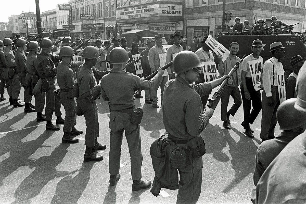 Striking sanitation workers and their supporters are flanked by bayonet-wielding National Guard troops and armored vehicles during a march on City Hall in Memphis, Tenn., on In this March 29, 1968.