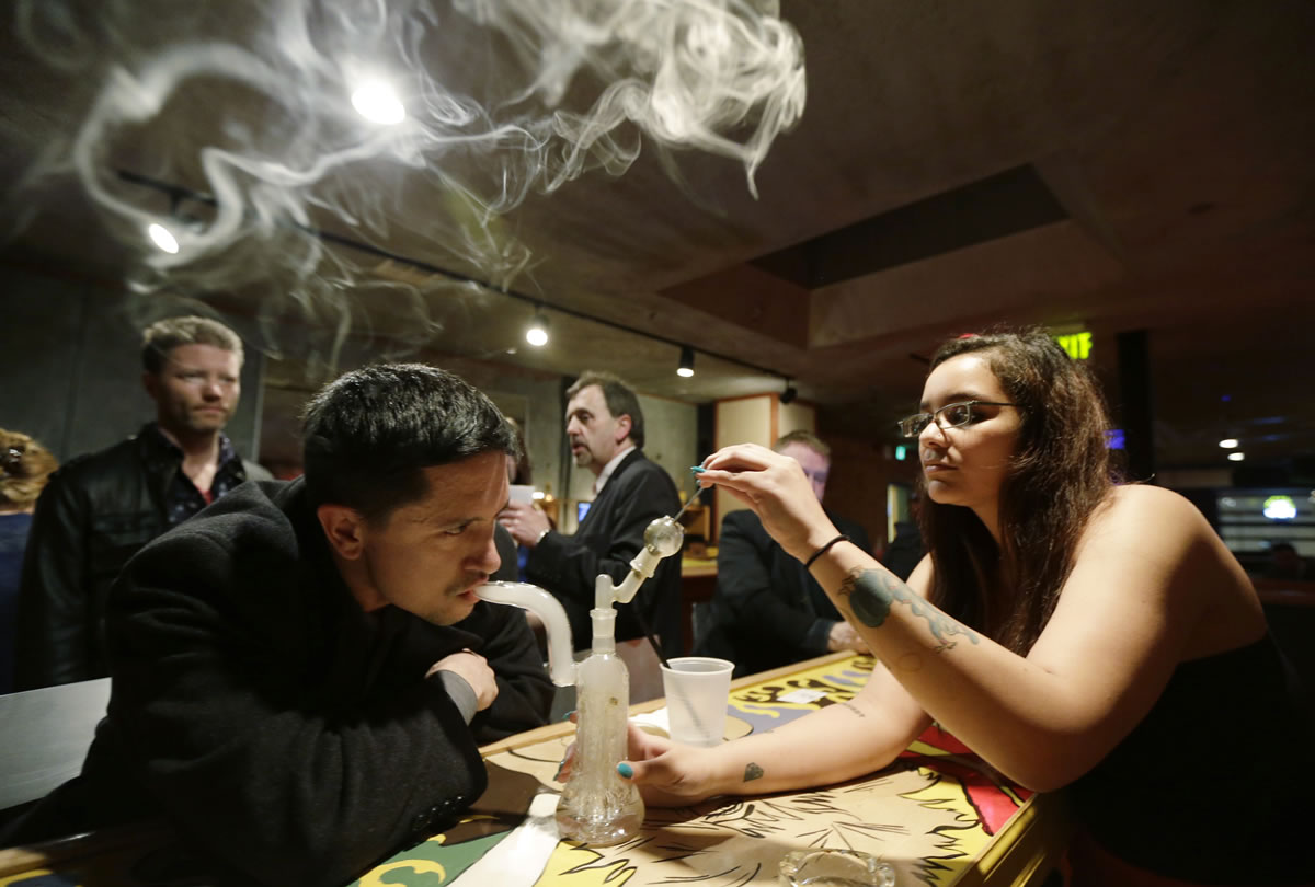 John Connelly, left, inhales marijuana vapor just after midnight March 2 with the help of bar worker Jenae DeCampo, right, in the upstairs lounge area of Stonegate, a pizza-and-rum bar in Tacoma.