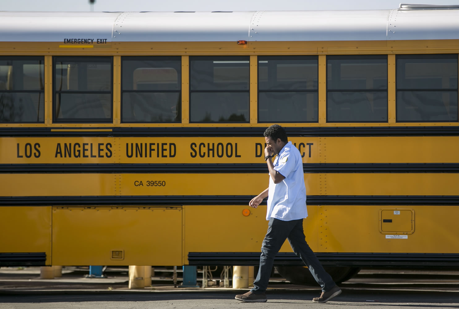 A Los Angeles Unified School District bus driver walks past parked vehicles at a bus garage in Gardena, Calif., on Tuesday.