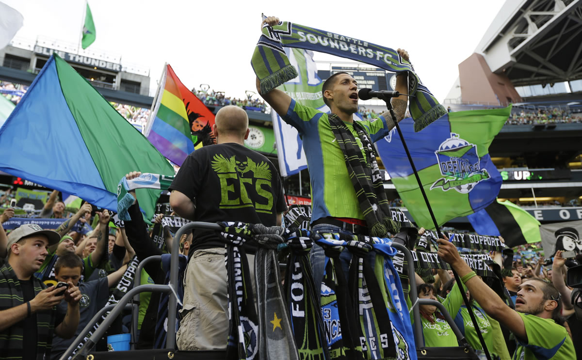 Clint Dempsey, right, captain of the United States Men's National Soccer Team, and the newest member of the MLS Seattle Sounders team, raises a Sounders scarf as he stands with supporters, Saturday in Seattle.