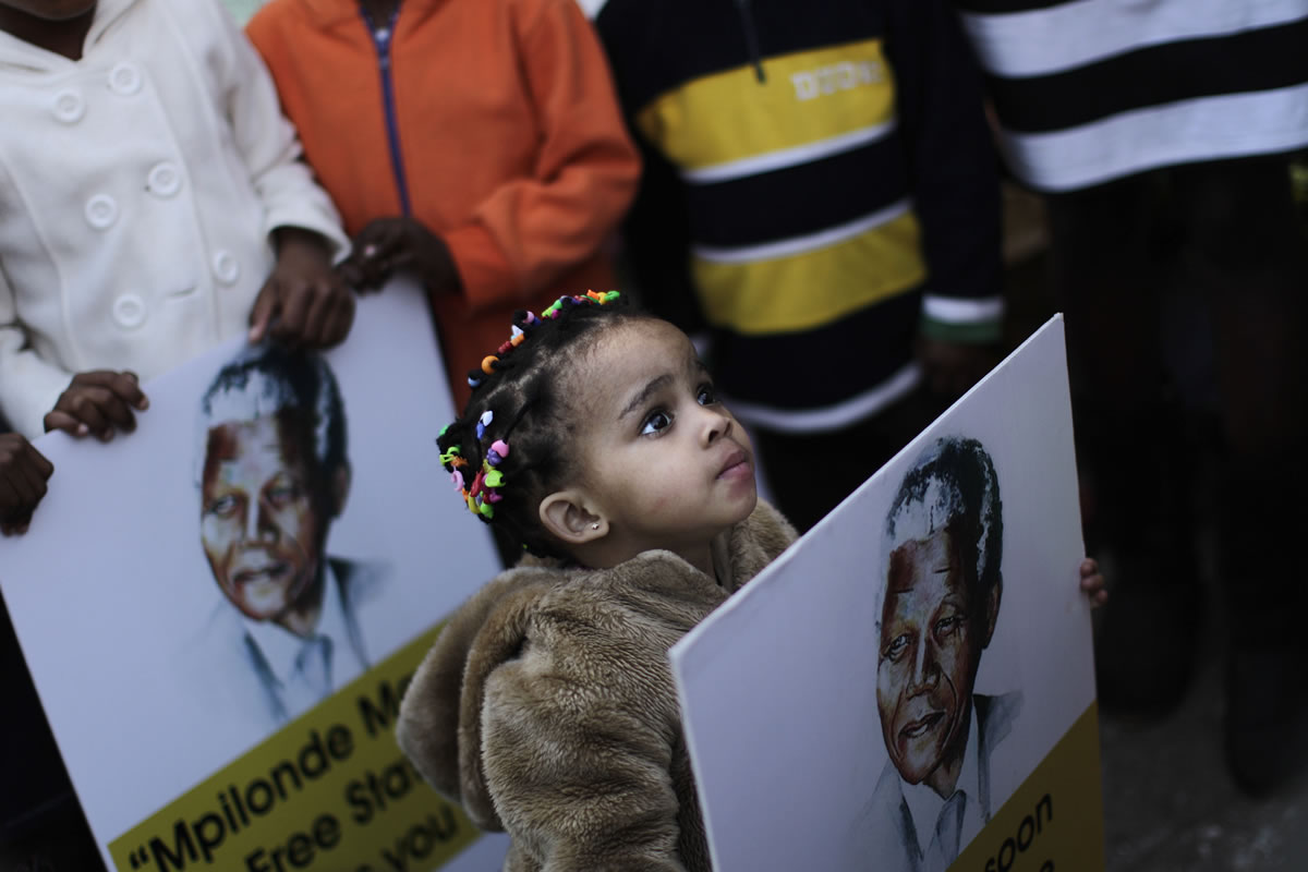 A South African girl holds a poster Friday showing former South African President Nelson Mandela, while her family and other well wishers gather at the entrance to the Mediclinic Heart Hospital where former South African President Nelson Mandela is being treated in Pretoria, South Africa.