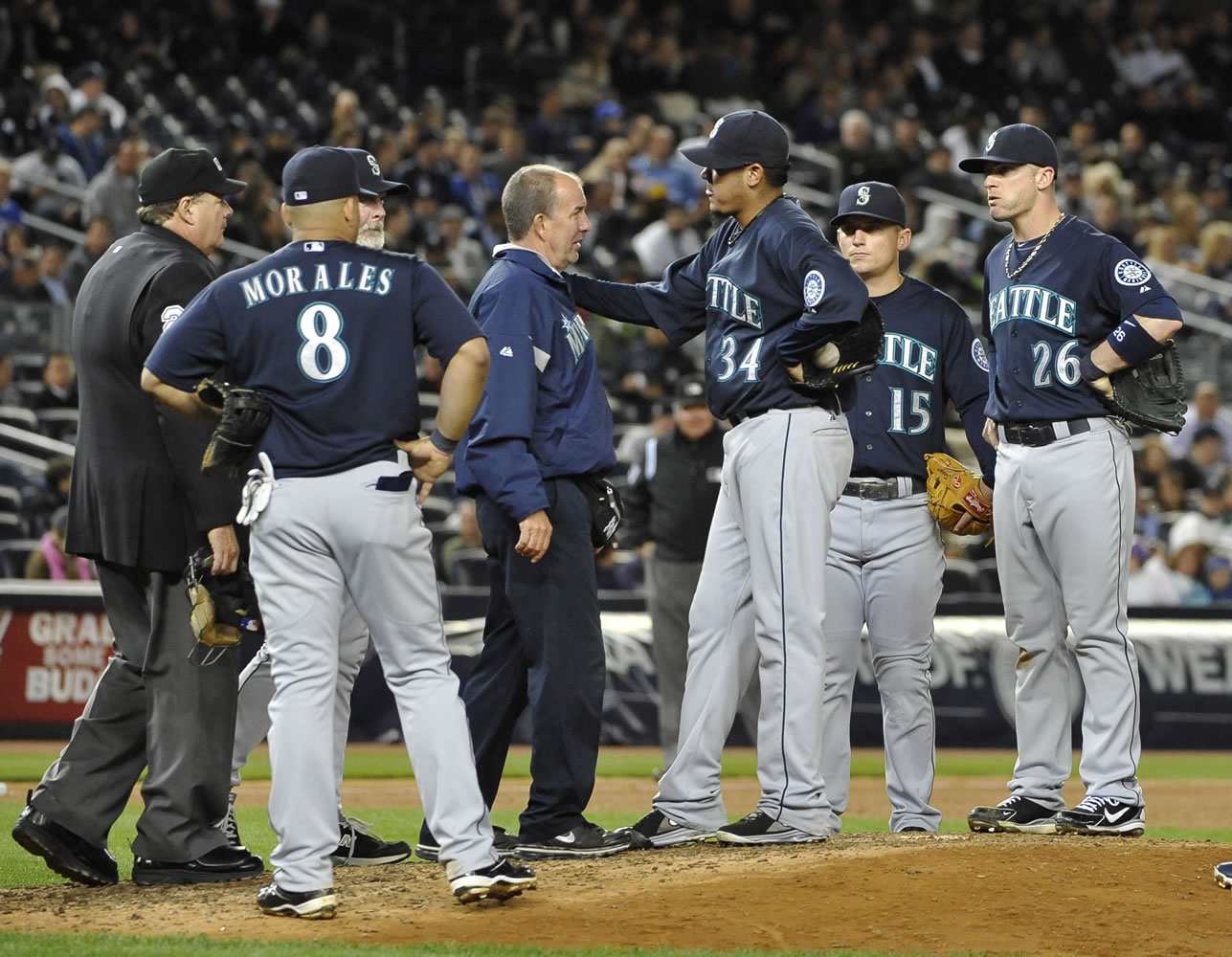 A Seattle Mariners trainer comes to the mound to check on starting pitcher Felix Hernandez (34) after the Mariners pitcher aggravated his sore back.